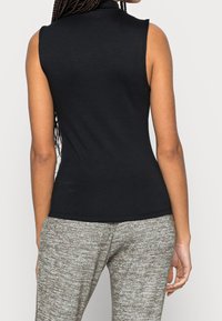 Svart ärmlös topp i mjukt tyg med hög halsringning och tight passform, kombinerad med ljusgrå strukturerade byxor.