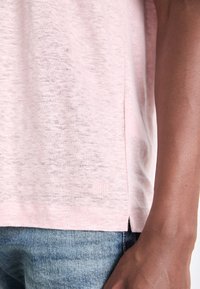 Ljusrosa kortärmad t-shirt i mjukt, strukturerat tyg. Har en liten logotyp nära fållen och sidoklyftor för ökad komfort.