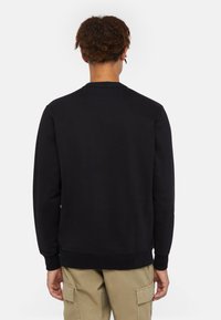 Felpa nera con maniche lunghe, polsini a coste, collo rotondo e una consistenza morbida. Abbinata a pantaloni cargo beige.