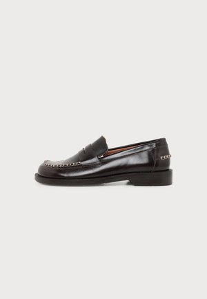 Zwarte leren loafer met gestikte moc-toe en decoratieve metalen kettingdetail op hiel en bovenkant, platte zool en lage hak.