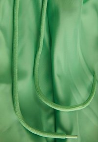Tessuto verde con una superficie liscia presenta un cordino coordinato e un bordo più ampio. Il materiale appare leggero e flessibile.