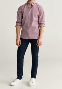 Camisa de botones a cuadros rojos y blancos, de manga larga, material de algodón, combinada con vaqueros oscuros y zapatillas blancas.