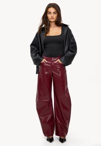 Zwarte leren oversized jas, aansluitende zwarte top en wijde bordeauxkleurige faux-krokodillenbroek. Tulpvormige zwarte hakken maken de look compleet.