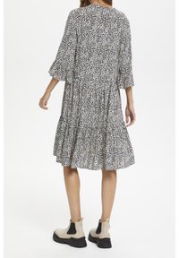 Midi šaty s vrstveným designem, s černobílým abstraktním potiskem. Dlouhé rukávy a lehká tkanina; doplněné béžovými kotníkovými botami.