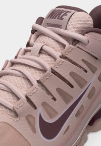 Κοντινό πλάνο ροζ αθλητικού παπουτσιού Nike που δείχνει υφασμάτινη υφή, κορδόνια, ενισχυτικές επιφάνειες και το λογότυπο Nike σε σκούρο μοβ χρώμα.