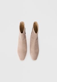 Béžové semišové kotníkové boty s špičatou špičkou, jemným švy a bočním zipem pro snadný přístup. Plná podrážka, minimalistický design.