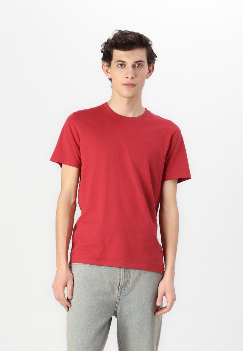 Rød bomull t-skjorte med korte ermer og rund hals, kombinert med lyseblå denimjeans. Enkel design, ingen synlige mønstre eller detaljer.