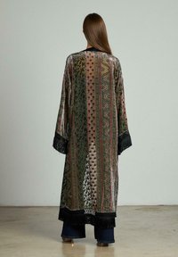 Kimono lung, ușor, cu modele intricate în verde, maro și aur, cu manșete franjurate negre și o formă largă, fluidă.