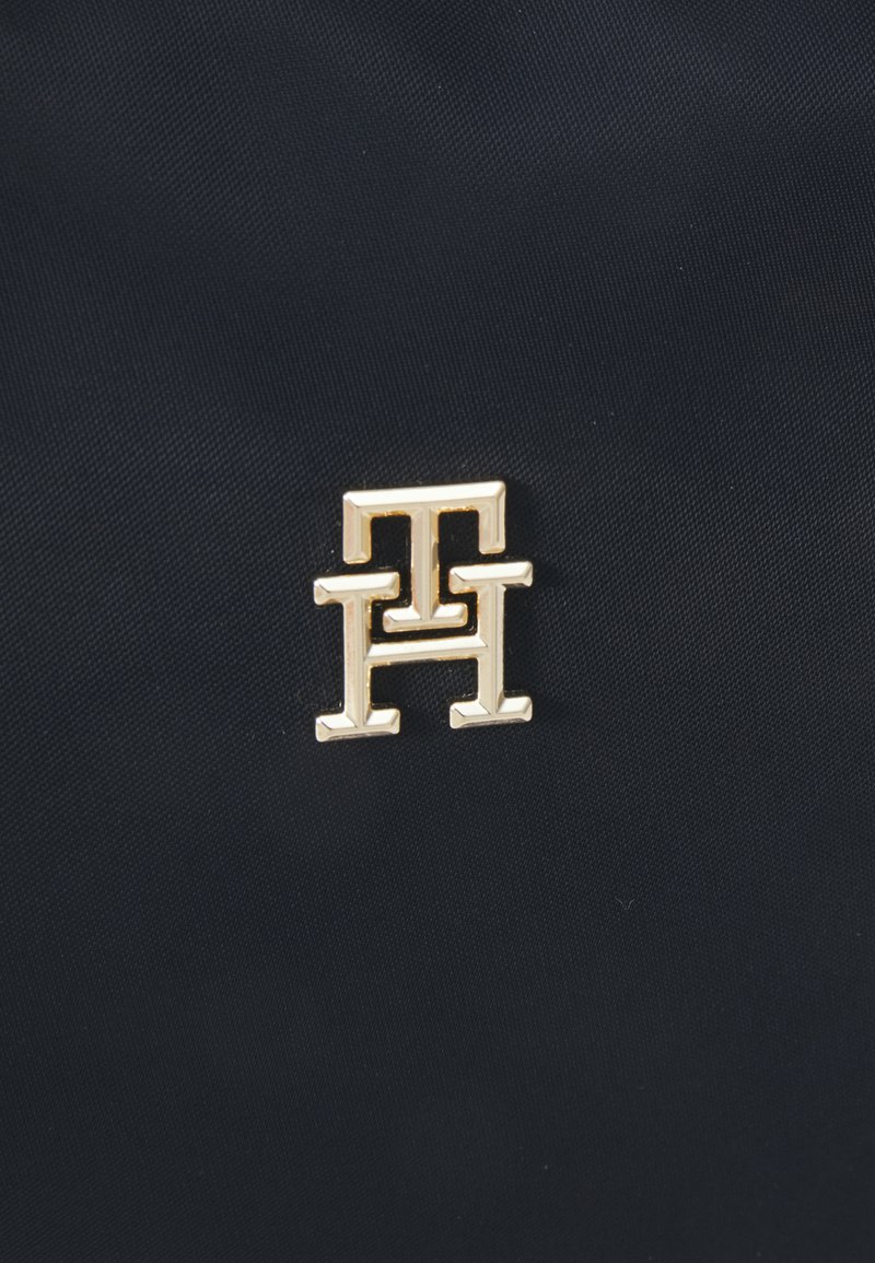 Sac en tissu bleu marine mettant en avant un logo doré proéminent avec des lettres entrelacées "T" et "H" embossées à la surface.