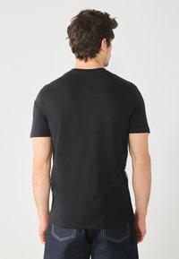 T-shirt en coton noir à manches courtes et col rond, avec une texture lisse et une coupe régulière. Porté avec un jean en denim foncé.