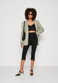 Grøn houndstooth blazer, sort cropped top, sorte leggings med blondekant, og sorte hælede mules, med solbriller og en håndtaske.