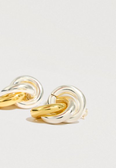 Μεταλλικά σκουλαρίκια με στριφτό σχέδιο σε ασημί και χρυσές αποχρώσεις, που αναδεικνύουν μια απαλή, γυαλιστερή υφή και διαδοχικούς συνδεδεμένους κρίκους.