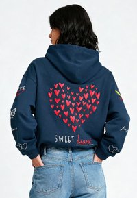 Marine hoodie met rood hartontwerp op de achterkant, voorzien van meerdere harten, geborduurde tekst "SWEET heart," en accenten op de mouwen.
