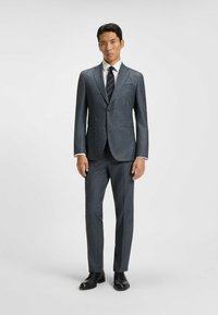Grijs patroon kostuum met een enkelvoudige blazer, wit overhemd en gestreepte stropdas. Zwarte schoenen maken de formele look compleet.