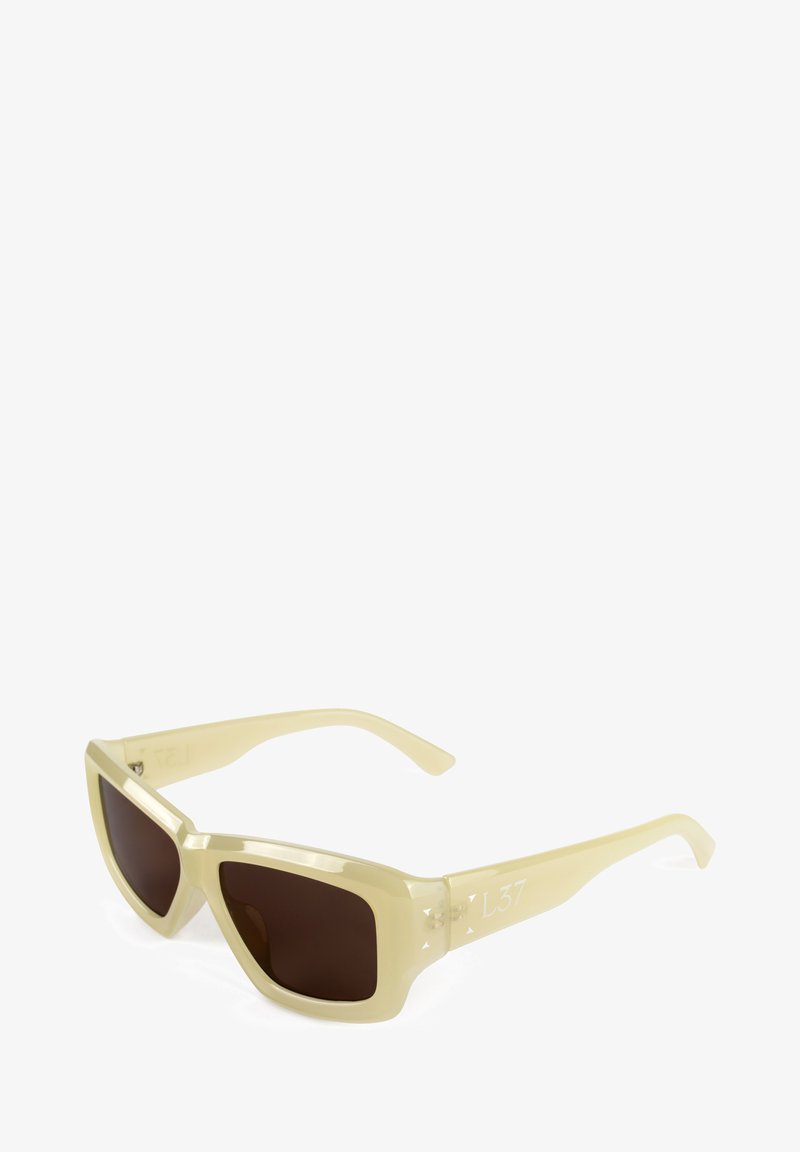Gafas de sol de plástico amarillo claro con lentes marrones, diseño angular y un discreto detalle del logo en el lateral. Patillas delgadas, acabado brillante.