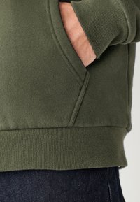 Donkergroene sweater met geribbelde manchetten en zoom, voorzien van een zijzak en een gladde, gestructureerde stof.