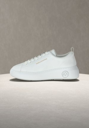 Witte lage sneaker met dikke zool, veters aan de voorkant, gouden tekst "Armani Exchange" aan de zijkant en "AX" logo op het hielplatform.