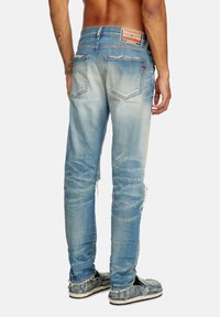 Faded blue denim jeans with ripped accents, slim fit, and a branded leather patch on the waistband, showcasing a light wash texture.