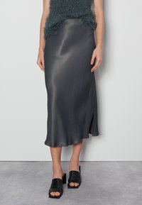 Dunkelgrauer Satin-Midikleid mit Seitenschlitz, leicht und mit glatter Textur, kombiniert mit schwarzen Mules mit Blockabsatz.