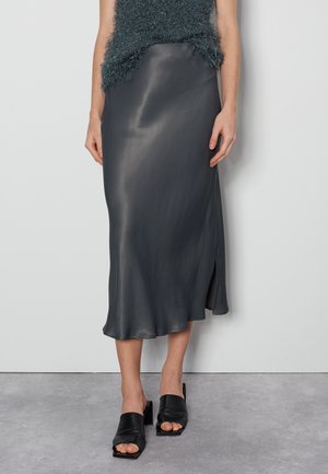 Gonna lunga in satin grigio scuro con uno spacco laterale, tessuto leggero e liscio, abbinata a mule con tacco largo neri.