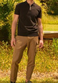 Ruskea vetoketjullinen pikeepaita neuloksesta, yhdistetty beigeihin cargo-housuihin joissa on sivutaskut, käännetyt lahkeet ja sileä pinta.