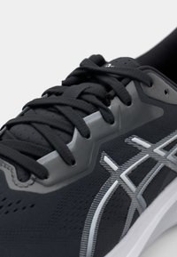 Czarne buty sportowe z teksturowaną cholewką, szarymi akcentami, wyraźnym systemem sznurowania oraz białą podeszwą środkową z widocznym logo.