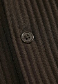 Tejido acanalado marrón con una textura vertical, que presenta un botón redondo oscuro con cuatro agujeros, fijo en el centro.