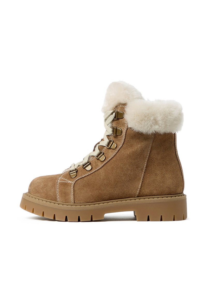Braune Wildleder-Stiefeletten mit einem flauschigen, cremefarbenen Fellkragen, Schnürung vorne, Metallösen und einer dicken, robusten Gummisohle.