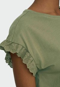 Ljust grön kortärmad topp med scallop-formad ögla och mjukt material. Har en avslappnad passform och rund halsringning.