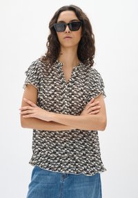 Blusa a maniche corte con motivo in bianco e nero, con bottoni frontali e leggero arriccio sulle spalle, abbinata a jeans in denim blu.