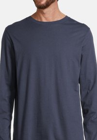 Maglietta a maniche lunghe blu navy realizzata in tessuto morbido con colletto a girocollo a costine e una texture liscia, che mostra la parte superiore del corpo di un modello.