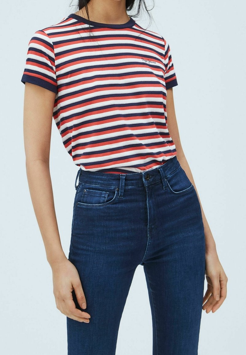 Rød, hvid og marineblå stribet kortærmet t-shirt med rund halsudskæring og broderet logo, parret med mørkeblå jeans.