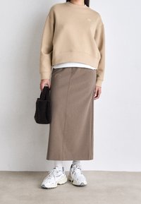 Beige oversized sweatshirt, brun midikjol och vita sneakers med grå detaljer. Svart texturerad handväska, lager på lager med en vit skjorta under.