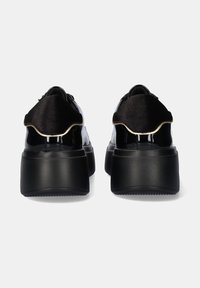 Zapatillas negras de plataforma con cuero charol brillante y suaves acentos de terciopelo, que presentan un tacón grueso y un diseño redondeado en la parte trasera.