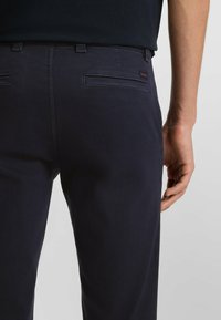 Pantalones color azul marino hechos de tela suave, con un corte clásico, dos bolsillos traseros y un sutil logotipo en la cinturilla.