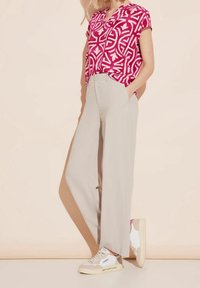 Růžová vzorovaná halenka s krátkými rukávy, doplněná světle béžovými širokými kalhotami a bílými teniskami s béžovými detaily a nápisem na podrážce.
