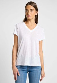 Camiseta blanca de cuello en V, de manga corta, ligera, con tejido ligeramente texturizado, de corte holgado, combinada con pantalones vaqueros azules, diseño sencillo.