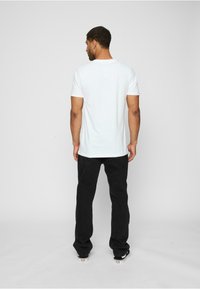 Hvid bomulds t-shirt til mænd med rund hals, parret med sorte strukturerede bukser, set fra ryggen. Casual pasform.