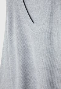 Pull en maille gris clair avec col en V et texture côtelée, présenté sur un fond uni.