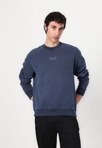 Felpa blu navy con scollatura rotonda, polsini e orlo a coste. Presenta un piccolo logo stampato sul petto. Realizzata in tessuto morbido.
