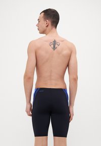 Shorts de bain noirs avec des accents bleus, offrant une coupe ajustée et une texture lisse. Le design comprend un motif sur le côté et un détail de logo.
