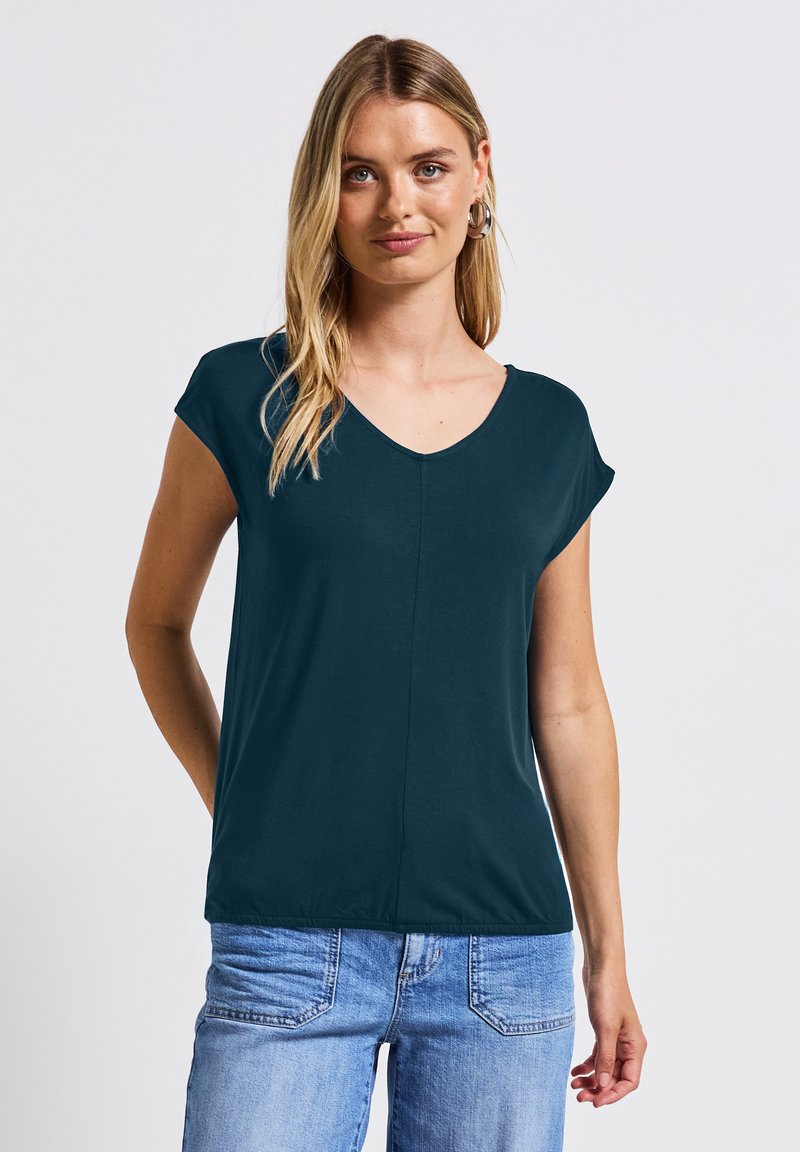 T-shirt noir-vert à col en v avec des manches courtes, texture douce et couture centrale. Associé à un jean bleu clair, coupe décontractée.