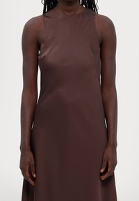 Braunes Satin-Kleid mit hohem Ausschnitt und ärmellosem Design, das eine glatte Textur und ein figurbetontes Oberteil aufweist, das in einen ausgestellten Rock übergeht.
