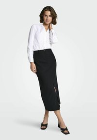 Witte blouse met knopen en een zwarte midi rok met streepjes en een zijsplit. Zwarte sandalen met blokhak maken de outfit compleet.