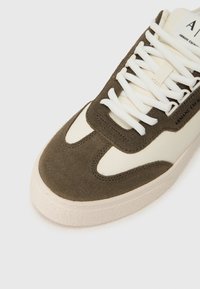 Creme- og brun ruskindssneaker fra Armani Exchange med hvide snørebånd og struktureret sål, vinklet for at vise top- og sidelayout.