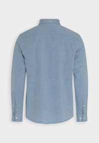 Chemise bleu clair à manches longues, avec col et ourlet arrondi, fabriquée en tissu texturé avec des poignets à boutons.