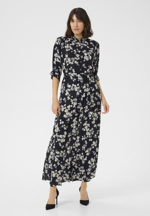 Floral maxi dress in navy with white and light pink flowers, button-down front, belted waist, and rolled sleeves. Worn with black heels.