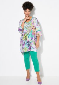 Flerfärgad tunika med tropisk tryck, parat med texturerade gröna byxor. Outfiten har en v-ringning och vida ärmar.