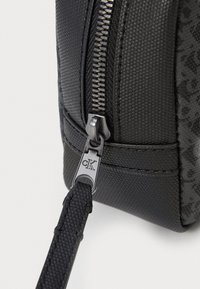 Bolso negro texturizado con una cremallera prominente con herrajes plateados, detalles laterales y un sutil acento de logo.