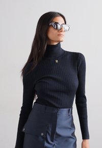 Sort ribbede turtleneck sweater med lange ærmer, der har en lille logo detalje. Kombineret med mørke højtaljede bukser.